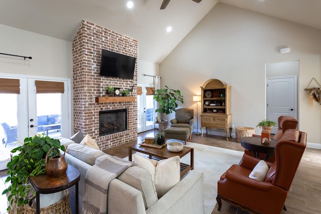 living room featuring ceiling fan, high vaulted ceiling, a brick fireplace, and wood finished floors