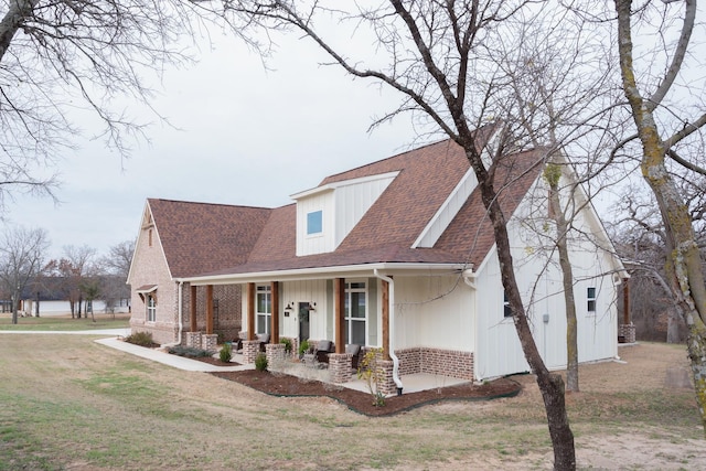 view of front of home with covered porch, brick siding, a shingled roof, and a front yard