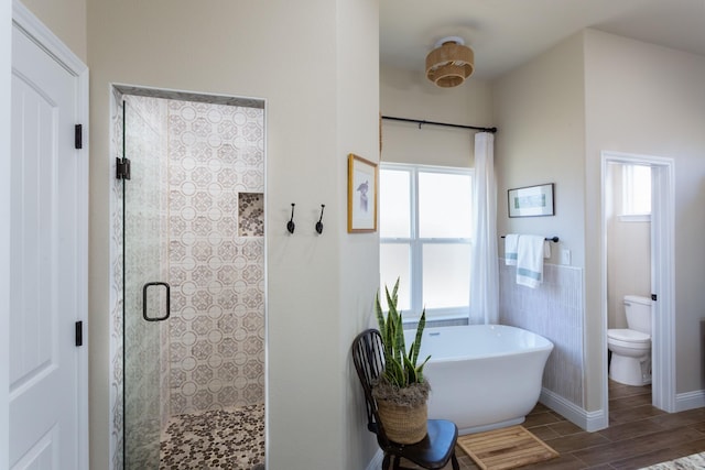 bathroom featuring a freestanding bath, toilet, a stall shower, wood tiled floor, and baseboards