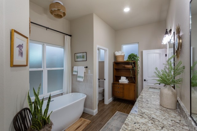 full bathroom featuring toilet, wood tiled floor, vanity, a freestanding tub, and baseboards