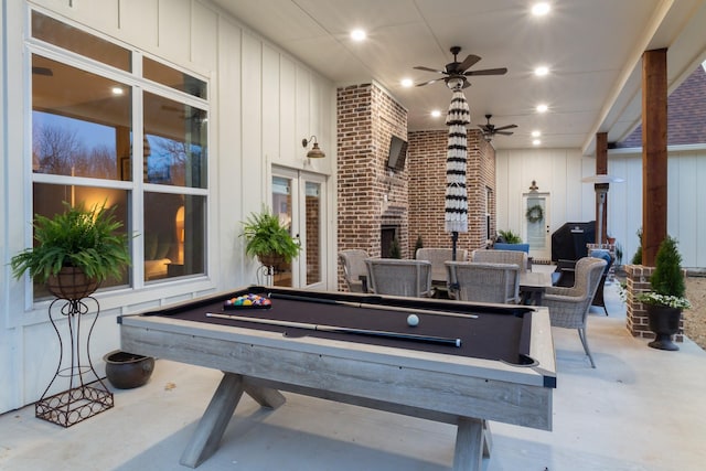 rec room featuring a ceiling fan, brick wall, pool table, an outdoor fireplace, and a decorative wall