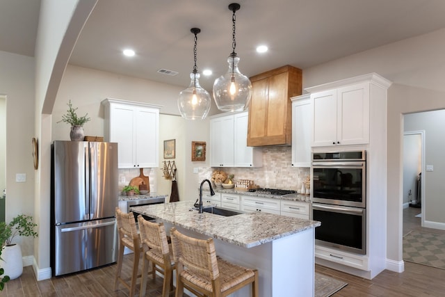 kitchen with visible vents, arched walkways, appliances with stainless steel finishes, a sink, and backsplash