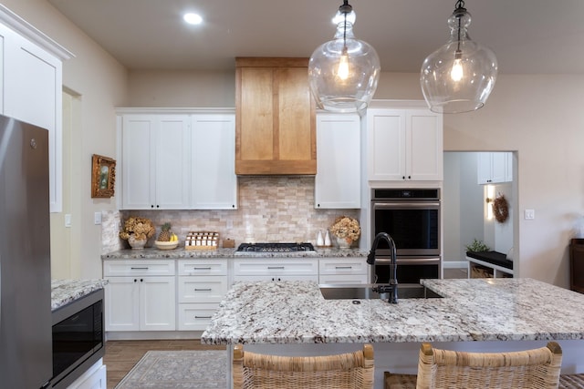 kitchen featuring decorative backsplash, a breakfast bar area, stainless steel appliances, white cabinetry, and a sink