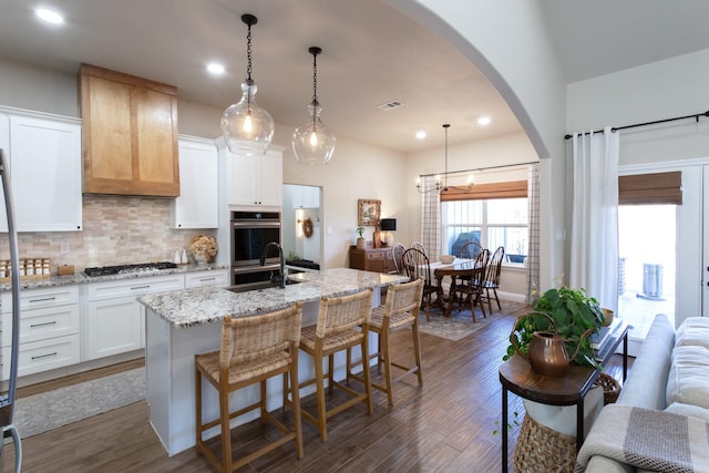 kitchen with light stone counters, dark wood finished floors, tasteful backsplash, appliances with stainless steel finishes, and a sink