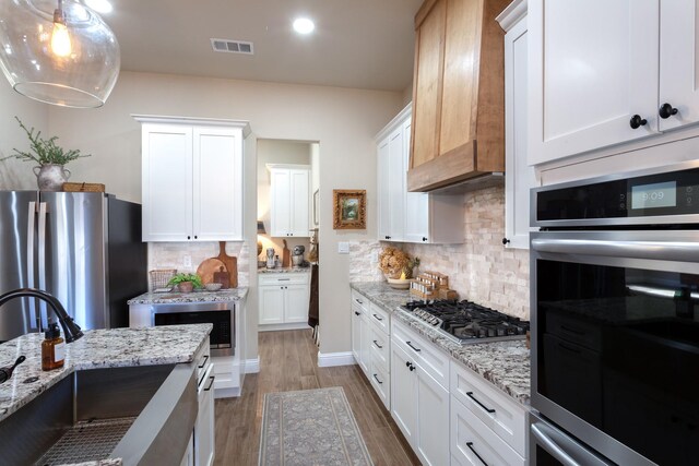 kitchen featuring stainless steel appliances, premium range hood, wood finished floors, a sink, and visible vents