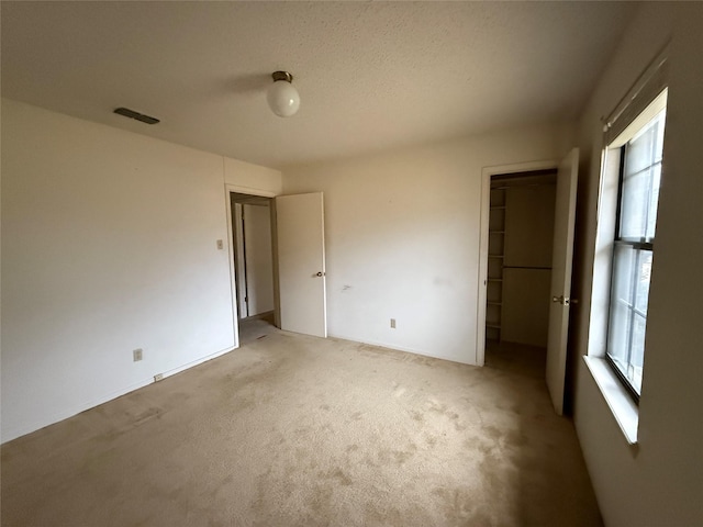 unfurnished bedroom featuring a closet, light colored carpet, visible vents, a spacious closet, and a textured ceiling