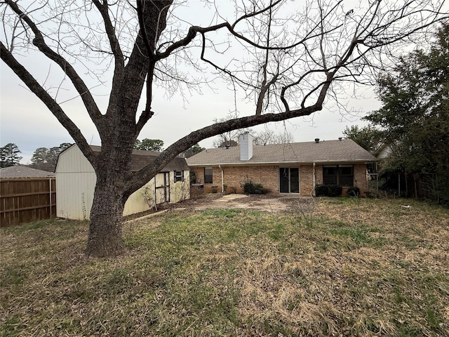 back of house featuring brick siding, a chimney, and fence