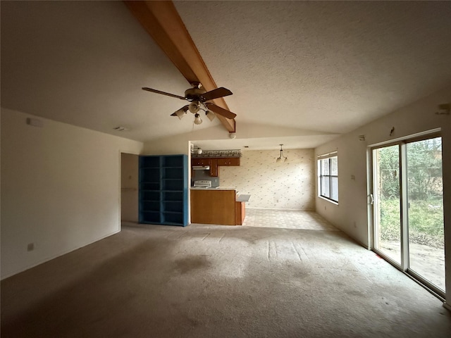 unfurnished living room featuring vaulted ceiling with beams, a textured ceiling, a ceiling fan, and light colored carpet