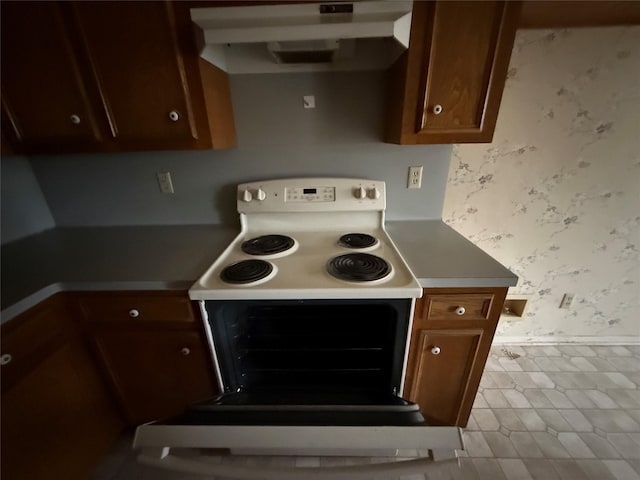 kitchen featuring wallpapered walls, under cabinet range hood, baseboards, and electric stove