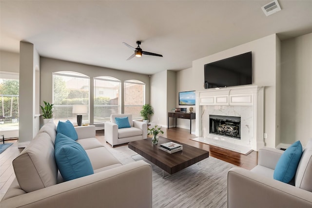 living area featuring visible vents, a premium fireplace, ceiling fan, wood finished floors, and baseboards