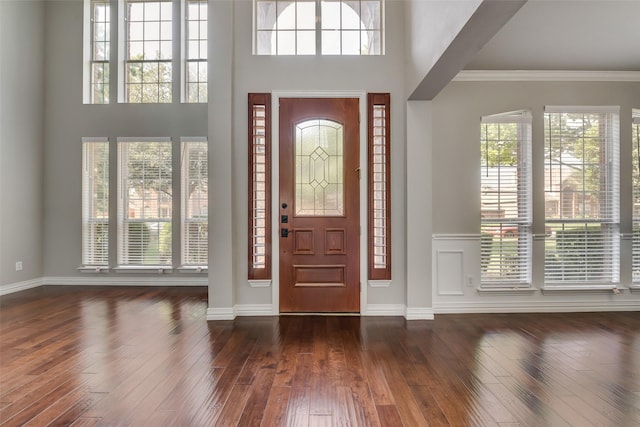 entryway with dark wood finished floors, a towering ceiling, and crown molding