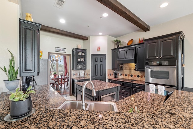 kitchen featuring tasteful backsplash, visible vents, beamed ceiling, double oven, and a sink