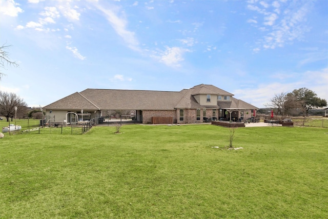 rear view of house featuring roof with shingles, brick siding, a patio, a lawn, and fence