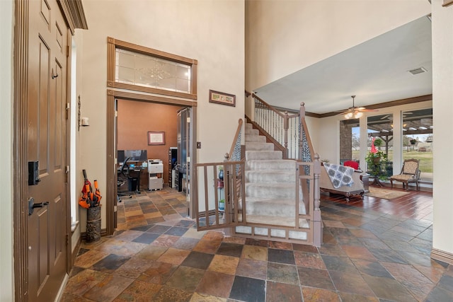 foyer with stone tile flooring, a towering ceiling, ceiling fan, baseboards, and stairs