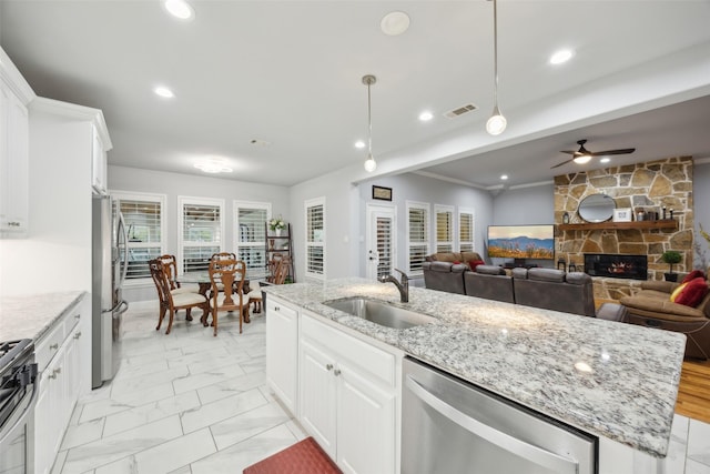 kitchen with visible vents, an island with sink, appliances with stainless steel finishes, a stone fireplace, and a sink