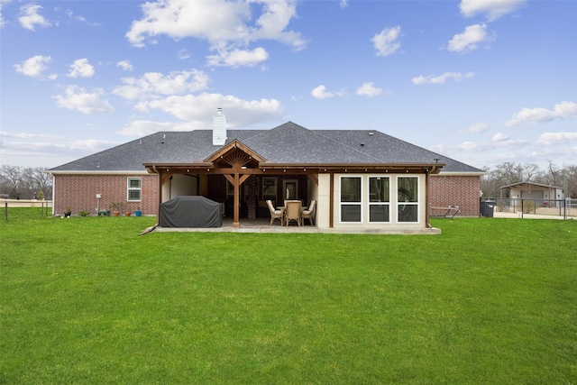 back of property featuring brick siding, a yard, a chimney, a patio area, and fence