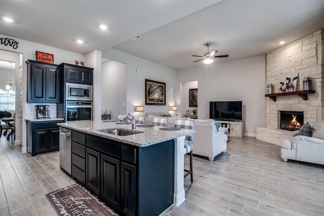 kitchen featuring appliances with stainless steel finishes, open floor plan, a stone fireplace, wood finish floors, and a sink