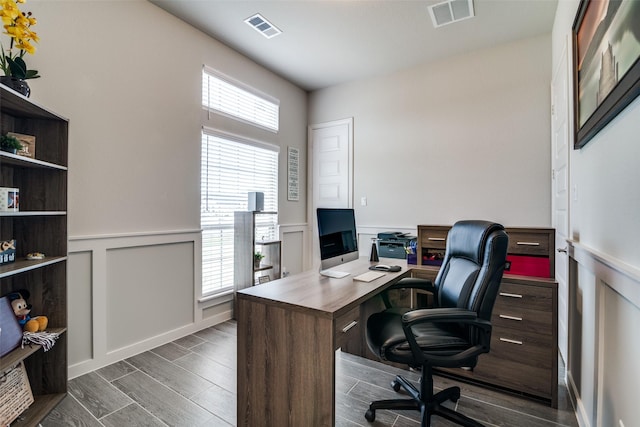 home office featuring wood finish floors, wainscoting, visible vents, and a decorative wall