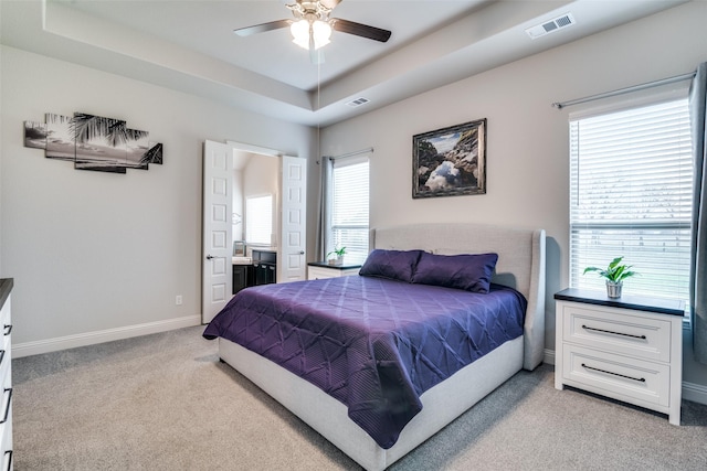 bedroom featuring light colored carpet, a tray ceiling, visible vents, and baseboards