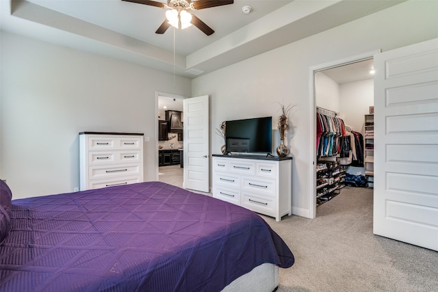 bedroom with a closet, a raised ceiling, light colored carpet, a spacious closet, and connected bathroom