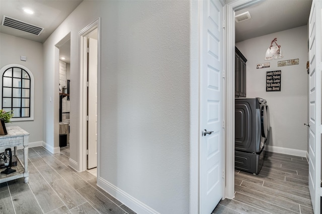 hall with baseboards, visible vents, wood finish floors, and independent washer and dryer