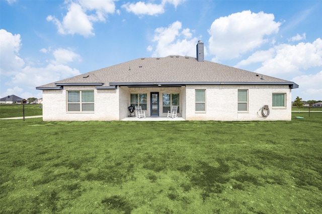 back of house featuring a chimney, fence, a lawn, and brick siding