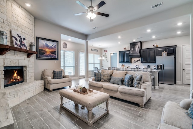 living room with a ceiling fan, wood tiled floor, visible vents, and a fireplace