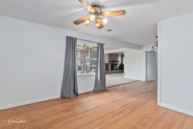 unfurnished room featuring ceiling fan, a textured ceiling, a fireplace, baseboards, and light wood-type flooring