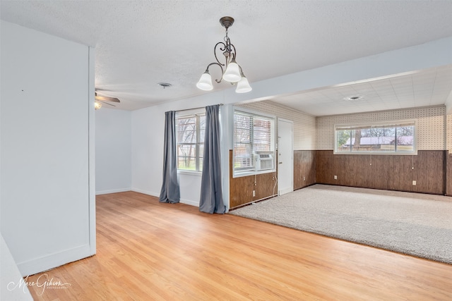 unfurnished room featuring a textured ceiling, a wainscoted wall, ceiling fan with notable chandelier, wood walls, and wood finished floors