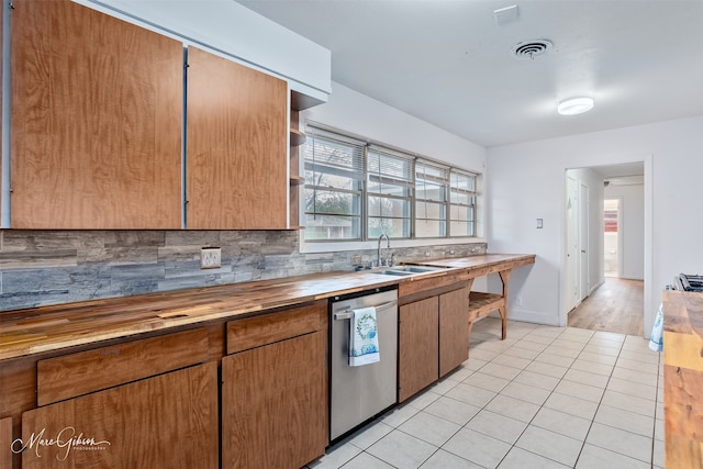 kitchen featuring light tile patterned floors, dishwasher, butcher block countertops, backsplash, and a sink