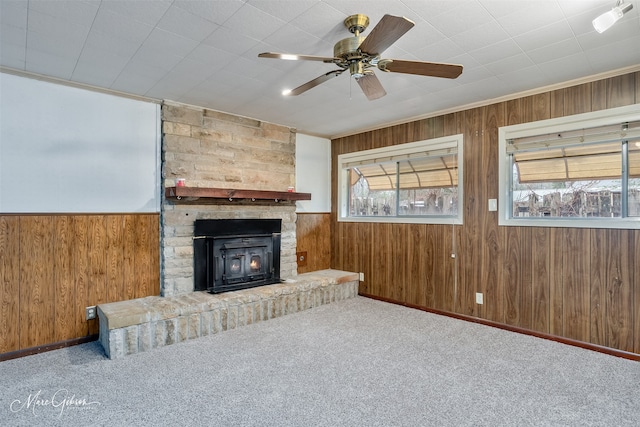 unfurnished living room featuring carpet floors, a fireplace, a ceiling fan, and wooden walls