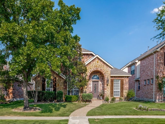 view of front of home featuring stone siding, a front lawn, a shingled roof, and brick siding