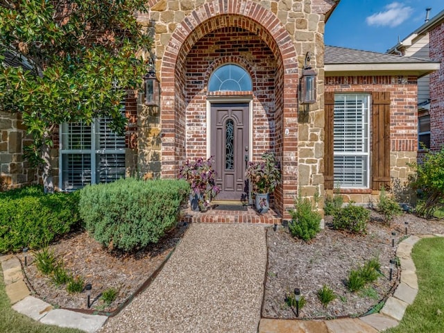 doorway to property featuring a shingled roof, stone siding, and brick siding