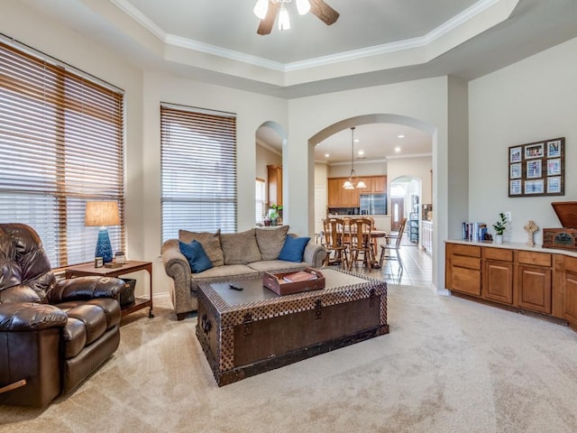 living room featuring arched walkways, light colored carpet, a ceiling fan, ornamental molding, and a tray ceiling