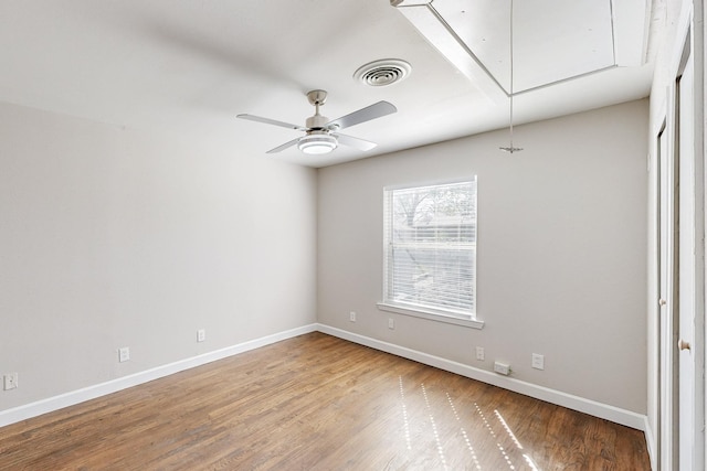 spare room with attic access, visible vents, baseboards, and wood finished floors