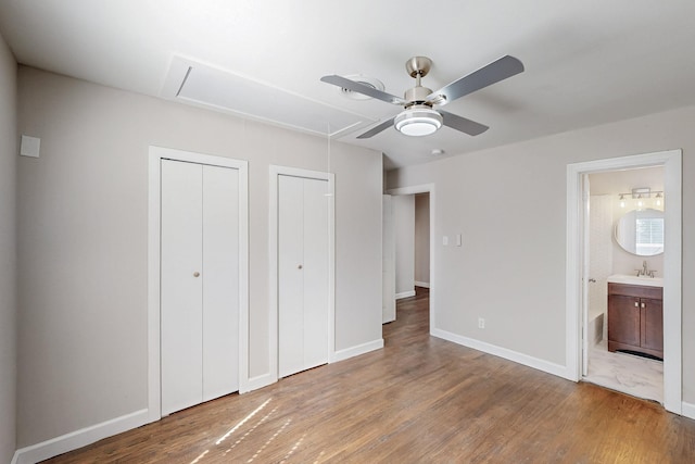 unfurnished bedroom featuring multiple closets, attic access, baseboards, and wood finished floors