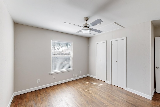 unfurnished bedroom with two closets, wood finished floors, attic access, and baseboards