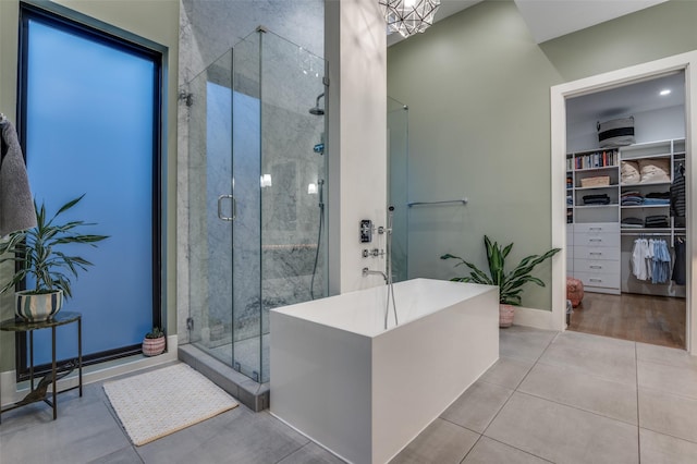 bathroom with a walk in closet, a freestanding tub, tile patterned flooring, and a shower stall