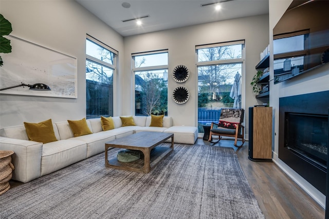 living room featuring a wealth of natural light, visible vents, wood finished floors, and a glass covered fireplace