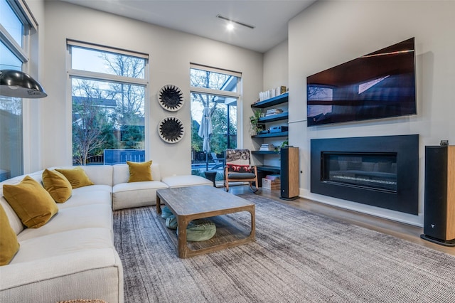 living area featuring wood finished floors, a glass covered fireplace, and visible vents