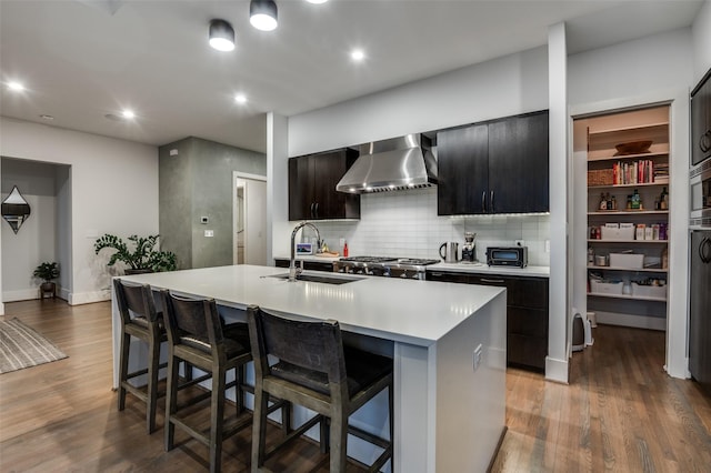 kitchen featuring a breakfast bar area, wood finished floors, light countertops, wall chimney range hood, and a sink