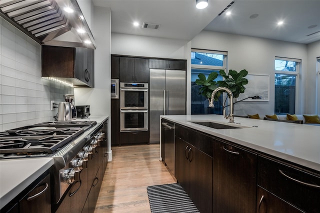 kitchen featuring wall chimney exhaust hood, stainless steel appliances, a sink, and light countertops