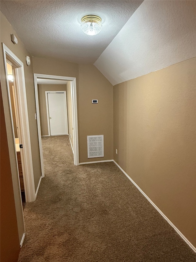 hallway featuring lofted ceiling, dark colored carpet, a textured ceiling, and visible vents