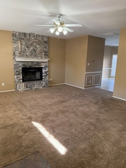 unfurnished living room featuring a large fireplace, baseboards, carpet floors, and ceiling fan