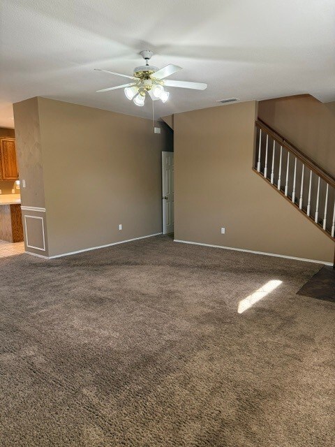 unfurnished living room featuring baseboards, visible vents, carpet floors, and ceiling fan