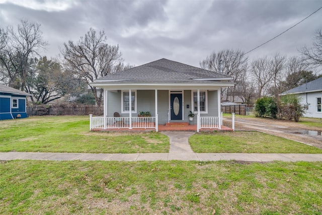 bungalow-style home with a shingled roof, a front yard, covered porch, and fence