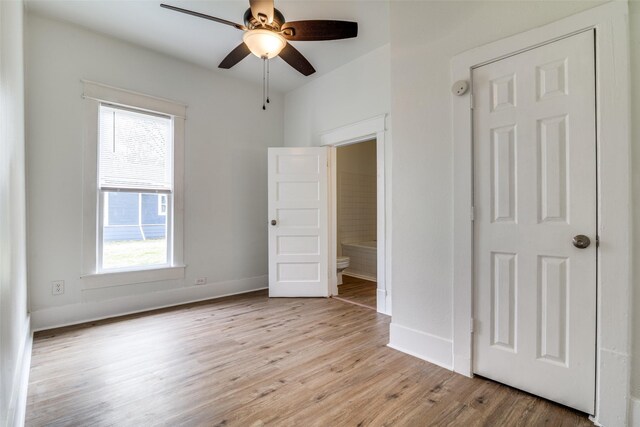 unfurnished bedroom with light wood-style floors, ensuite bath, baseboards, and a ceiling fan