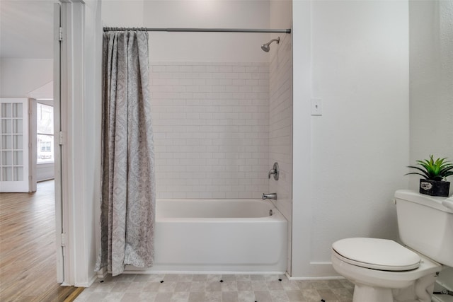 bathroom with toilet, shower / tub combo, and baseboards