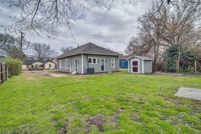 rear view of property featuring a lawn, a storage unit, fence, an outdoor structure, and central AC