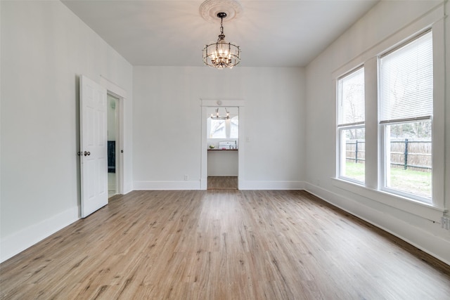 empty room featuring a chandelier, baseboards, and light wood finished floors